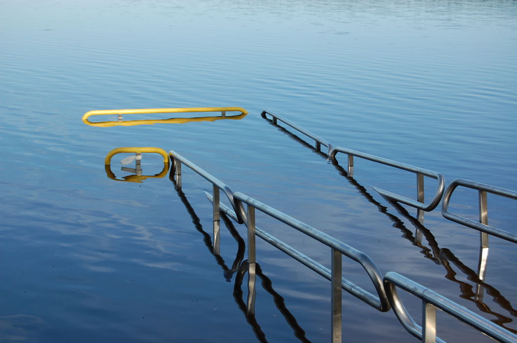 Närbild på EasyTrail-badramp med räcken och gul markering, utgång till vänster. Del av Floattechs tillgänglighetslösning för bad.