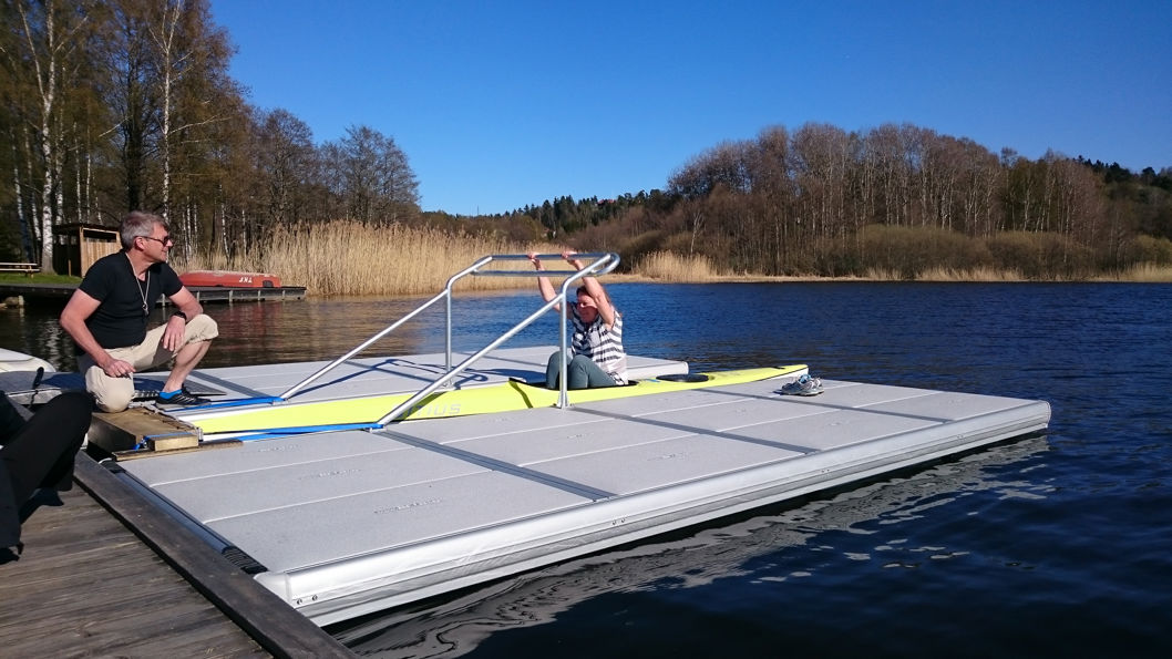 Man en vrouw bij een kano- of kajakclub gebruiken een toegankelijke leuning tussen twee EasyFloat steigers om gemakkelijk in en uit hun boten te stappen