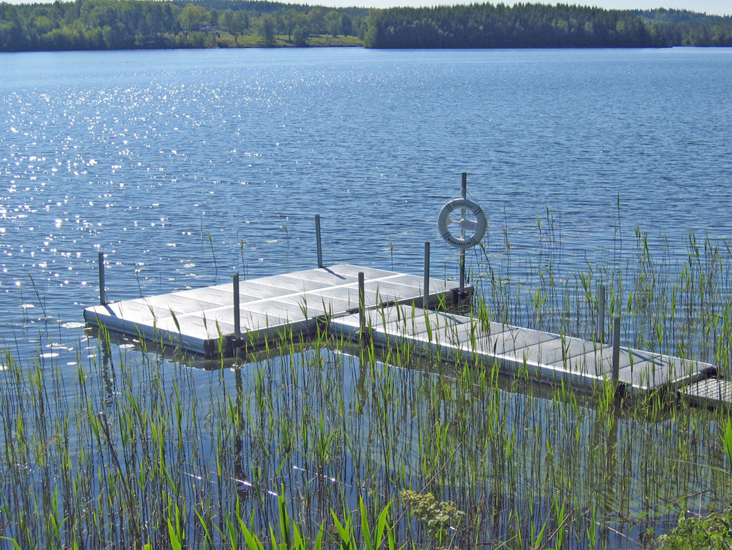 EasyFloat floating dock with lifebuoy by reeds. Sunlight sparkles on the blue water on a summer day.